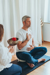 A man meditating with a sound bowl, and woman holds it during a calming sound therapy session