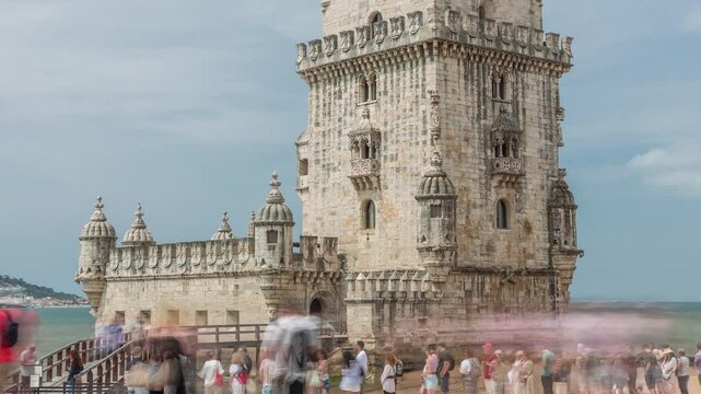 Torre de Belem or Belem Tower and wooden bridge timelapse hyperlapse on the Rio Tejo in Belem district of the City of Lisbon in Portugal. Long queue waiting for the entrance. Cloudy sky