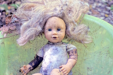 one gray brown dirty old doll toy lies on a green plastic table on a summer street