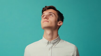 Fototapeta premium Thoughtful Young Man Looking Up Against a Turquoise Background