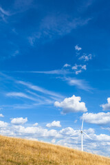 Agriculture and Wind Power Background / Harvested Field under blue cloudy sky with wind energy generator turbine (copy space)