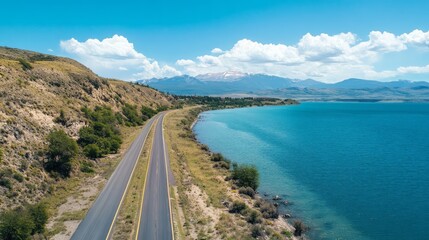 Obraz premium Scenic Coastal Road Along a Turquoise Lake with Mountains in the Background
