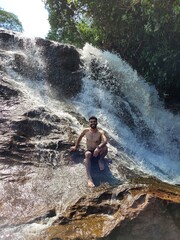 Young Man Posing Near a Waterfall in a Scenic Natural Setting with Trees and Fresh Air