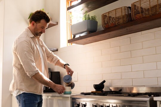 senior man pouring coffee in kitchen, enjoying morning sunlight at home
