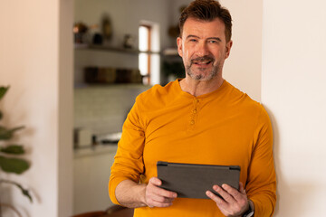 Smiling senior man holding tablet at home, enjoying relaxed holiday moment