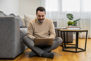 Fototapeta premium Man Sitting On Floor Working On Laptop in Cozy Living Room