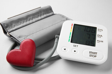 Blood pressure measuring device and heart figure on light grey background, closeup