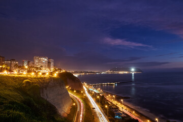 Fototapeta premium La Costa Verde under the night sky.The city lights dance along the coast, waves softened into mist with the long exposure, creating a dreamscape that feels otherworldly. Miraflores at night captures.