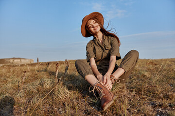 Woman in a hat relaxing on grassy field with hands in pockets enjoying a peaceful moment in nature