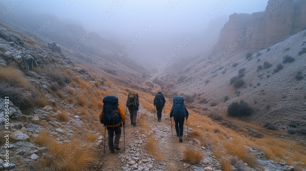 Poster hikers traverse a narrow trail through a fog-covered valley, surrounded by rocky cliffs and sparse v