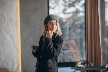 Fototapeta premium Young adult woman, a model, beautiful and happy in a cafe by the window with a cup of coffee