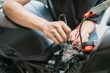 Obraz premium Motorcycle mechanic check motorcycle electrical system find wiring problems using a multimeter. work in garage, motorcycle repair concept ,