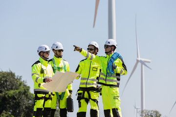 Fototapeta premium Group of male engineer wearing safety uniform working at wind turbines farm, discussing and planning maintenance of wind turbines at windmill field farm