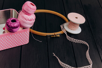 Assorted yarn and sewing tools in a pink tin box on a black wooden background create a visually...