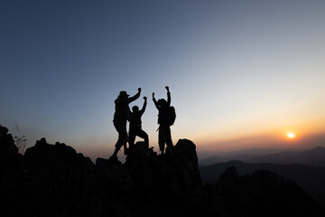 Fototapeta premium Silhouette of Together overcoming obstacles with three people holding hands up in the air on mountain top. climbing team work success business concept. growth and success.