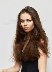 Fototapeta premium Young woman with long hair looking confidently at the camera, wearing a simple black top, against a light grey background. Beauty and self-expression concept.