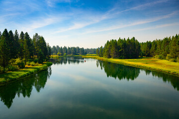 Fototapeta premium 2024-09-10 THE DESCHUTES RIVER WITH A BEAUTIFUL REFLECTION IN THE WATER AND A GRASS AND TREE LINED SHORE IN SUNRIVER OREGON