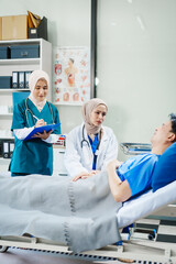 Obraz premium Two Muslim female doctors check the medical history and symptoms of a male patient lying in bed after surgery at the hospital, monitoring his recovery and health status