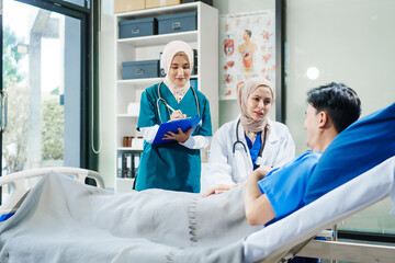 Obraz premium Two Muslim female doctors check the medical history and symptoms of a male patient lying in bed after surgery at the hospital, monitoring his recovery and health status