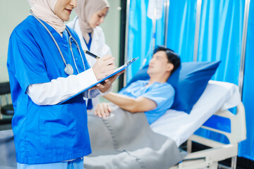 Obraz premium Two Muslim female doctors check the medical history and symptoms of a male patient lying in bed after surgery at the hospital, monitoring his recovery and health status