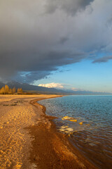 Sunset on the shore of Lake Issyk-Kul, Kyrgyzstan, with soft sandy beaches and a cloudy sky against...