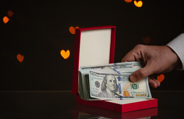 Man hand holding bundle of money on background of hearts