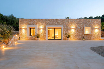 Modern stone house with warm lighting in a serene outdoor setting during dusk