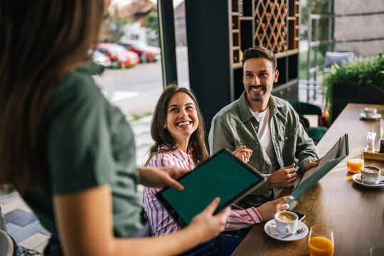 Group of people ordering food from the waitress. Waitress writing orders down on tablet. Undecided people reading the menu while the waitress waits and helps them.