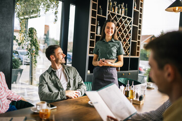 Group of people ordering food from the waitress. Waitress writing orders down on tablet. Undecided people reading the menu while the waitress waits and helps them.