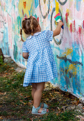 Fototapeta premium A little girl is painting a wall with a brush