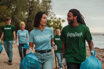 Two volunteers in uniforms talking and carrying waste by the river