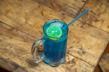 Blue mojito with lemon piece, blue mojito placed in a wooden dining table with blue color straw
