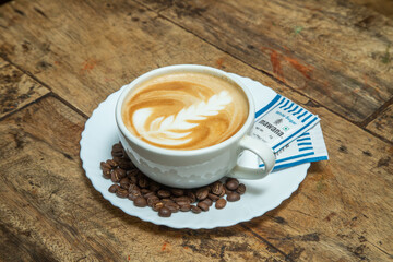 cappuccino cafes in a white cup with leaf shaped and brown colored along with chocolate dips and sugar packets