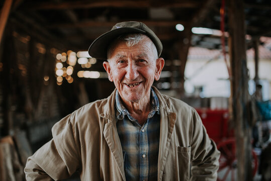 Old man wearing a hat and trench coat smiling.
