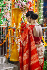 A traditional Bengali woman wearing a red saree joins her hands in a prayer position with closed...