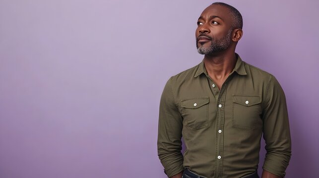 Portrait of a Reflective and Thoughtful Middle Aged Nigerian Man Dressed in a Casual Olive Green Henley Shirt and Dark Wash Jeans Posing Against a Plain Lavender Studio Background - Powered by Adobe