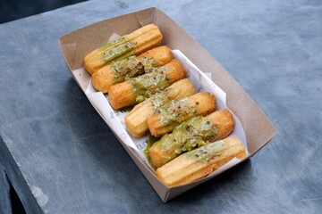 Crispy fried churros topped with savory green tea sauce, served in a paper-lined cardboard tray....