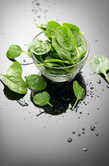 Spinach in a transparent glass bowl on gray background with reflection. Heap of Baby spinach fresh leaves close up, water drops, Healthy vegan food, diet, dieting, vitamin concept, vertical image 