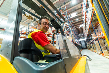 Happy manual worker driving forklift in distribution warehouse