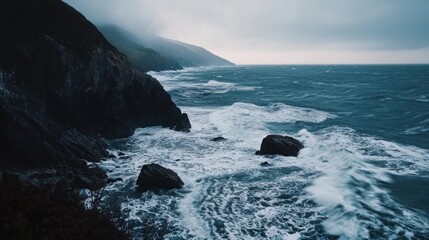 Dramatic ocean waves crash against rocky cliffs on a cloudy day.