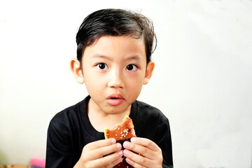 Young boy enjoying a delicious musubi, a traditional Japanese rice snack wrapped in nori and filled with savory ingredients. His curious gaze adds charm, capturing the joy of eating new foods.