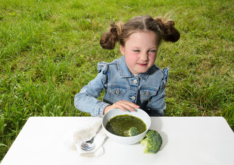The girl child refuses to eat broccoli soup.