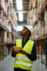 Warehouse worker checking stock with digital tablet and looking up at shelves