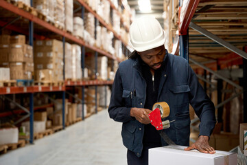 Warehouse worker sealing cardboard box with packing tape dispenser