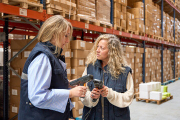 Female warehouse workers discussing using barcode scanners in logistics center