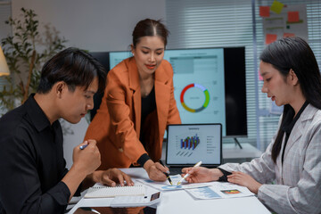 Fototapeta premium Three young asian professionals are reviewing data and brainstorming, collaborating on a project during a late night meeting at the office