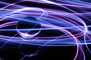 A long exposure photograph. Light painting photography. Swirls of colourful light behind and around a glass ball on a mirror.