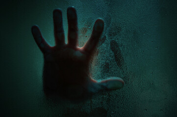 Horror scene of a hand against wet shower glass. Hand pressing against glass wall indoors. Toned...