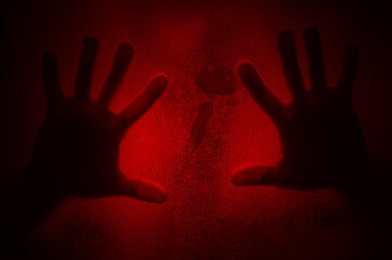 Horror scene of a hands against wet shower glass. Two hands pressing against glass wall indoors. Toned image.