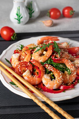 Salad with shrimps, arugula, cherry tomatoes, sweet peppers and sesame seeds on white plate